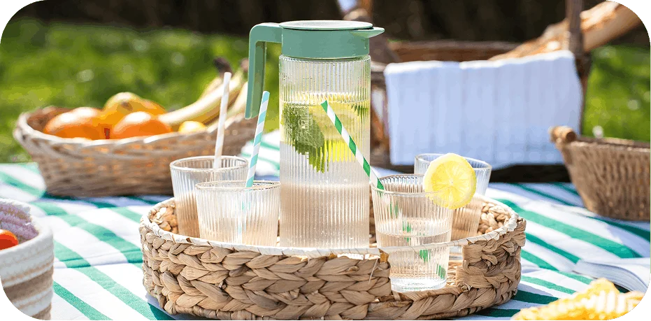 Carafe en verre nervuré et ses quatre verres offerts par Chronodrive, posés sur un plateau en osier lors d'un pique-nique
